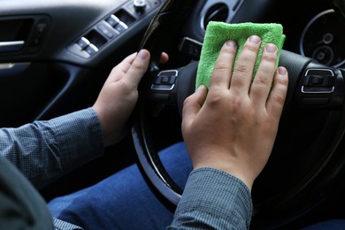 Photo of Man cleaning steering wheel with rag in car, closeup