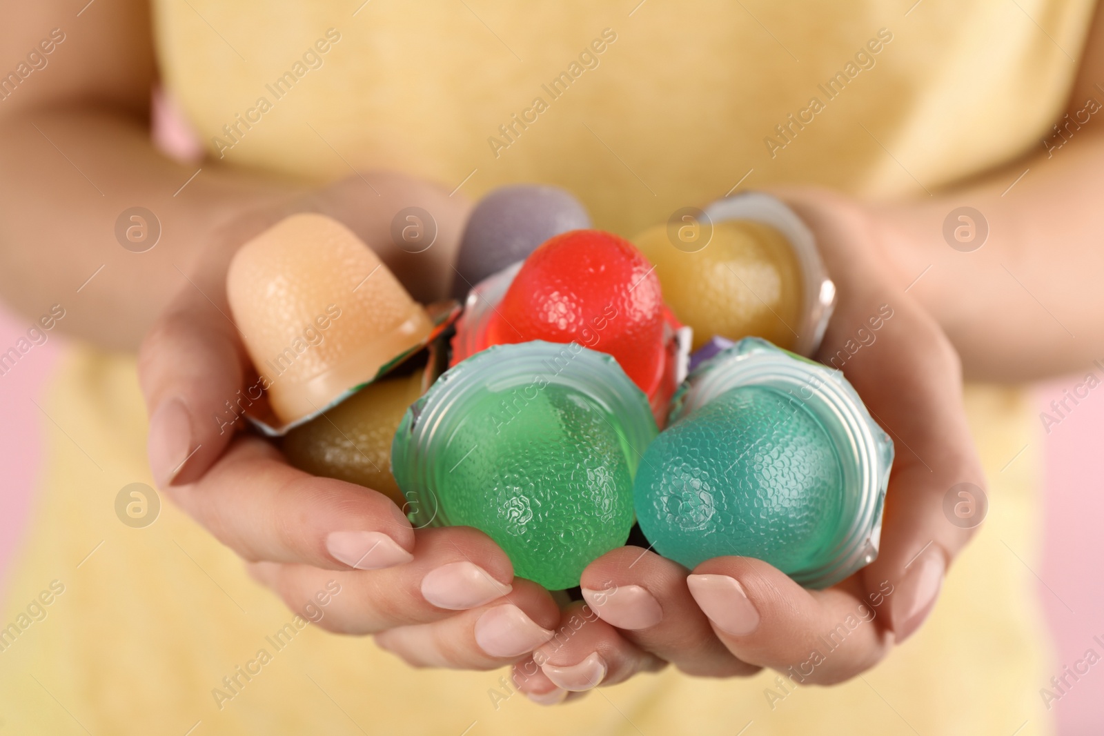 Photo of Woman holding many tasty bright jelly cups on pink background, closeup