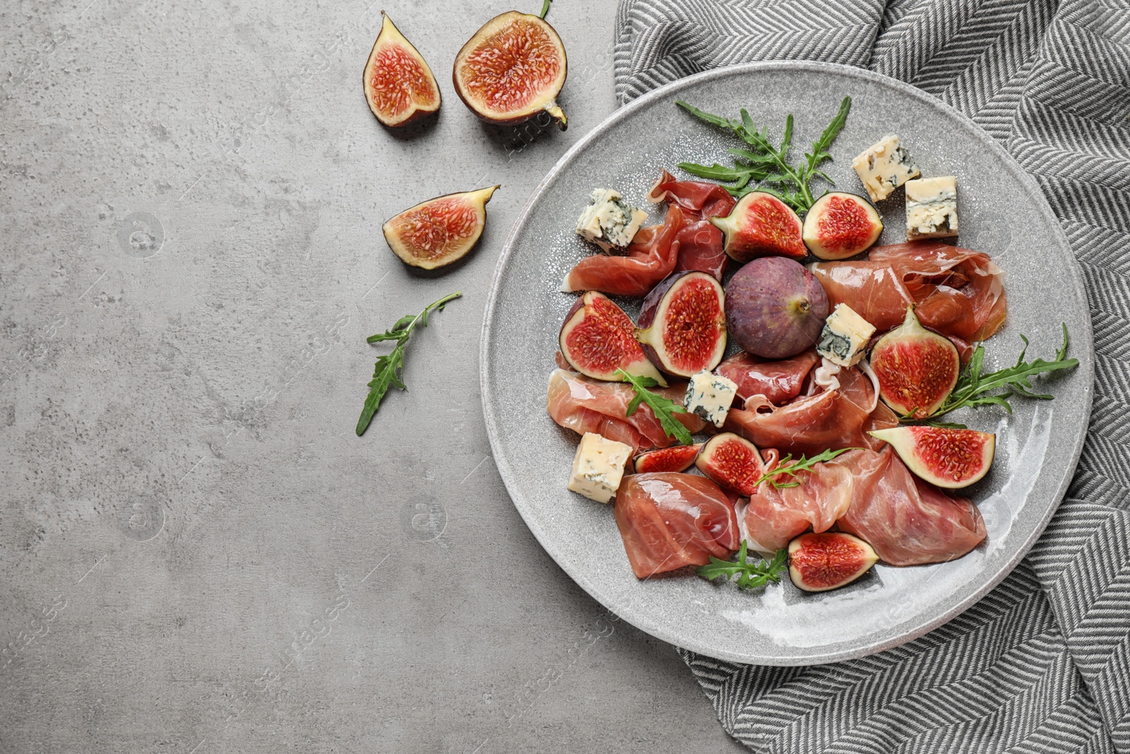 Photo of Plate with figs, prosciutto and cheese on light table, top view. Space for text