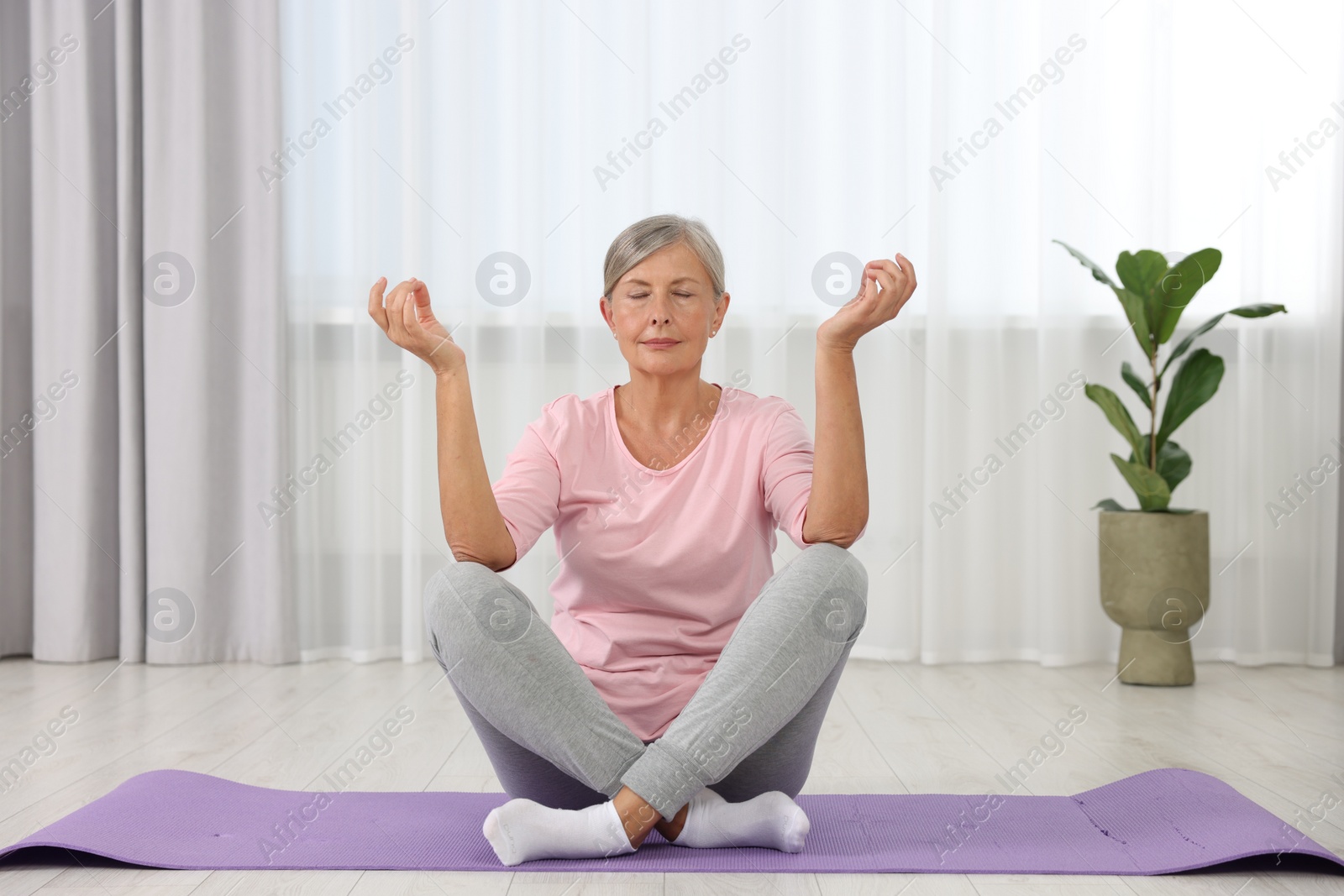 Photo of Senior woman practicing yoga on mat at home