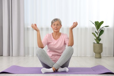 Senior woman practicing yoga on mat at home