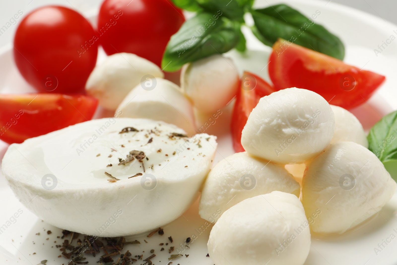 Photo of Delicious mozzarella with tomatoes and basil leaves on white plate, closeup