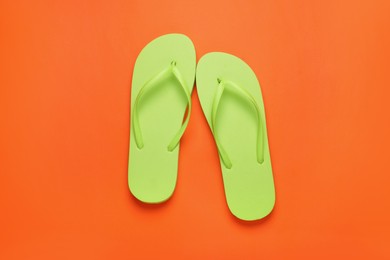 Stylish light green flip flops on orange background, top view