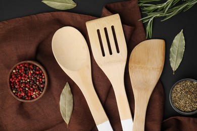 Photo of Set of wooden kitchen utensils and spices on black table, flat lay