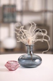 Vase with dried plant and candle on white table in room