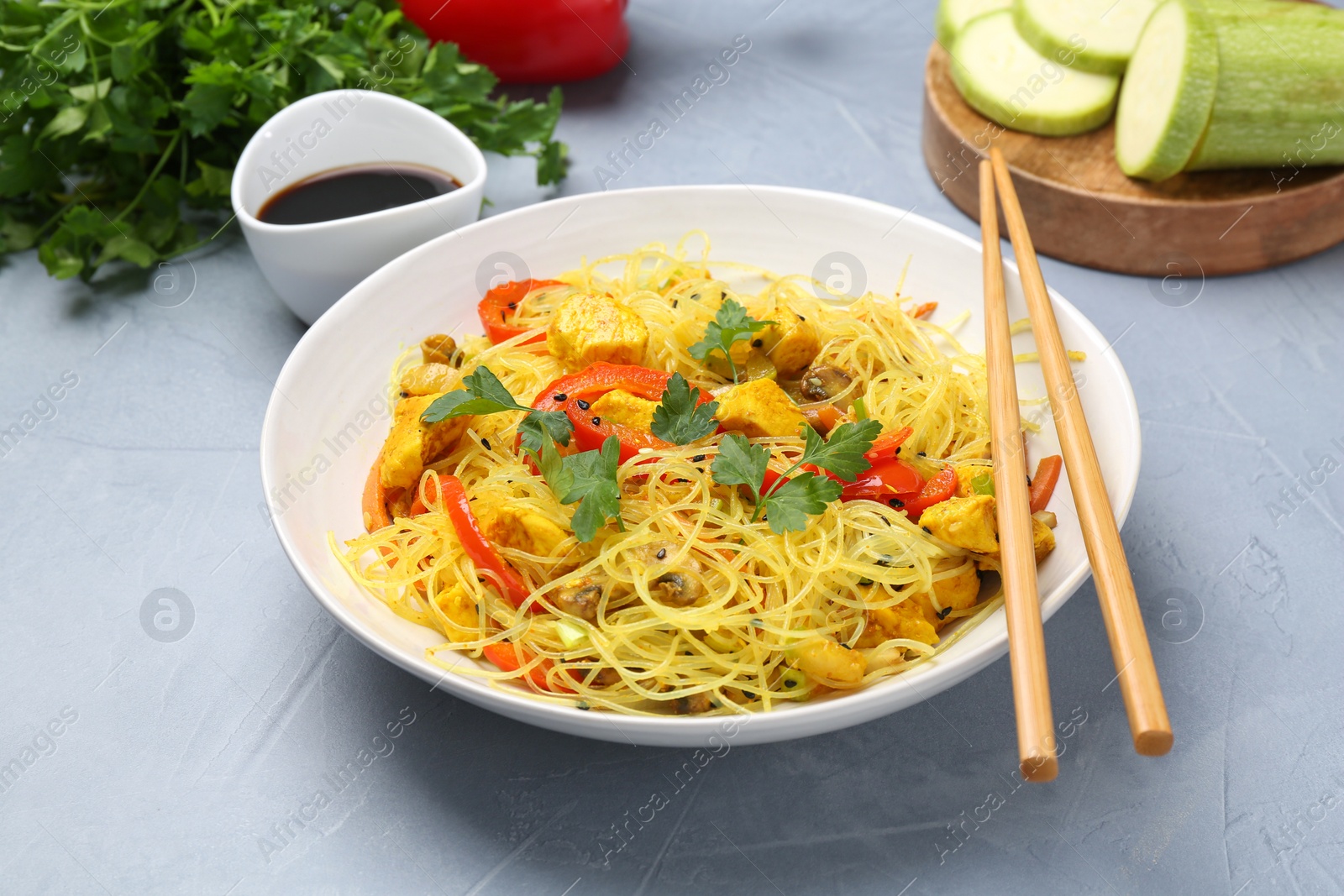 Photo of Stir-fry. Delicious cooked noodles with chicken and vegetables in bowl served on gray textured table