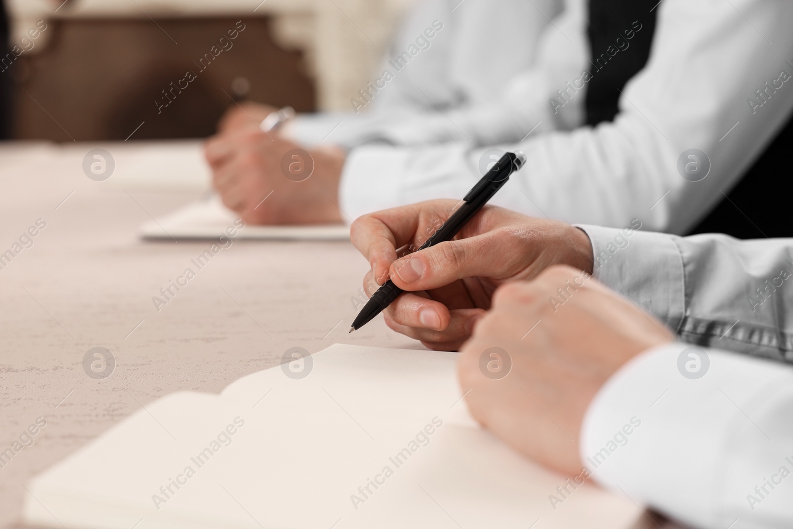 Photo of People writing notes in notebooks at table during lecture, closeup. Professional butler courses