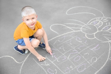 Photo of Little child drawing bunny with colorful chalk on asphalt