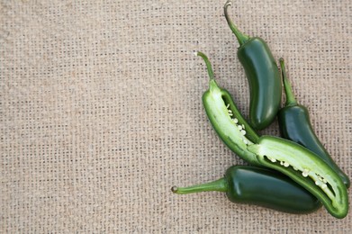 Photo of Whole and cut fresh green jalapeno peppers on sacking, flat lay. Space for text