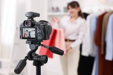 Photo of Fashion blogger with shopping bags recording video at home, focus on camera