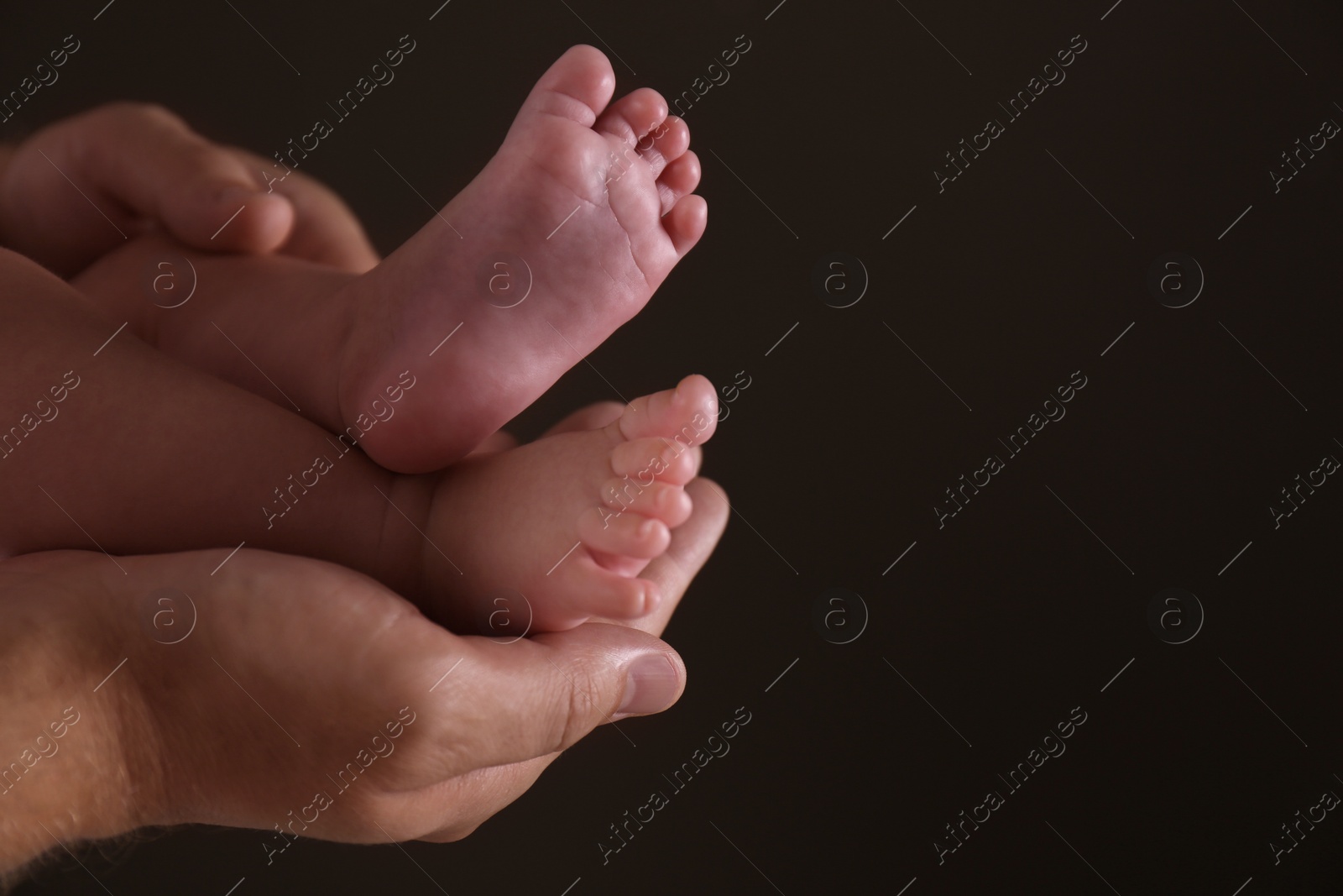 Photo of Father holding his baby against dark background, closeup. Space for text