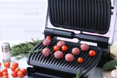 Photo of Electric grill with meatballs, tomatoes and rosemary on white table