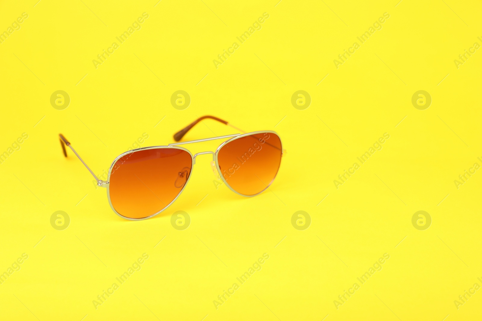 Photo of New stylish sunglasses on yellow background, space for text