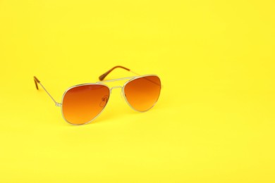 Photo of New stylish sunglasses on yellow background, space for text