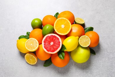 Photo of Pile of different fresh citrus fruits and leaves on grey textured table, flat lay