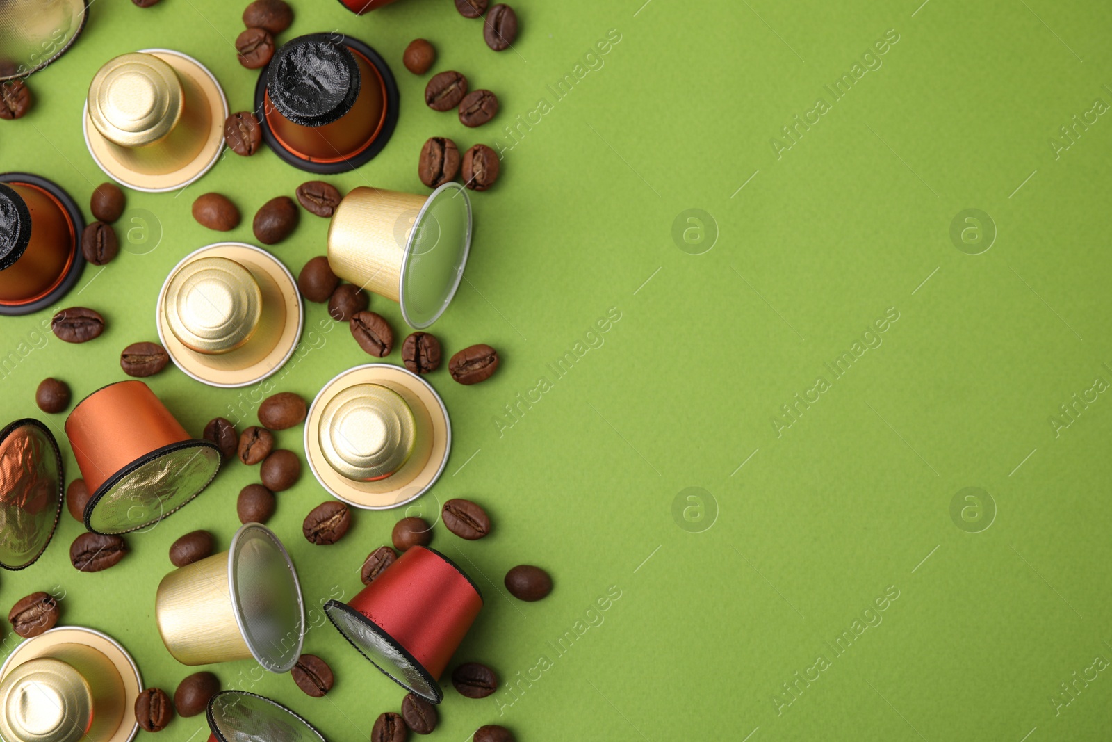 Photo of Many coffee capsules and beans on green background, flat lay. Space for text