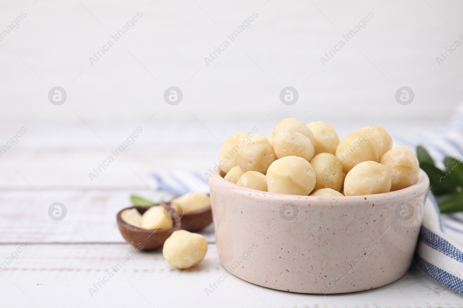 Photo of Tasty peeled Macadamia nuts in bowl on light table. Space for text