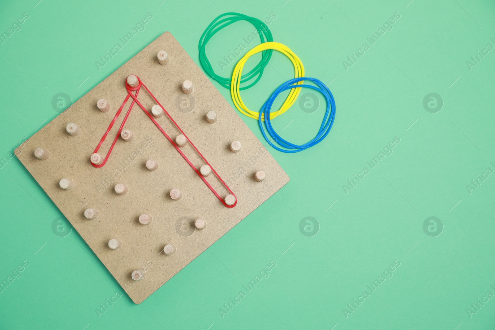 Photo of Wooden geoboard with rubber bands on green background, flat lay with space for text. Educational toy for motor skills development