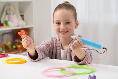 Girl drawing with stylish 3D pen at white table indoors