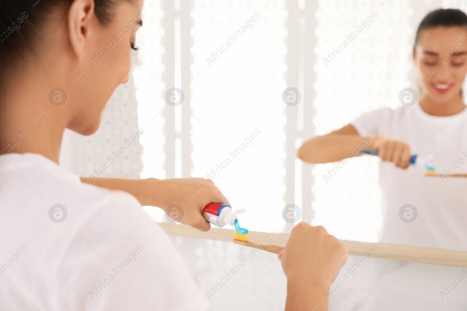 Photo of Woman applying toothpaste on brush in bathroom