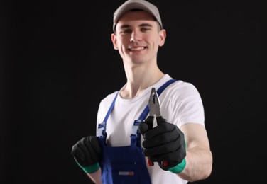 Photo of Young man holding pliers on black background, selective focus