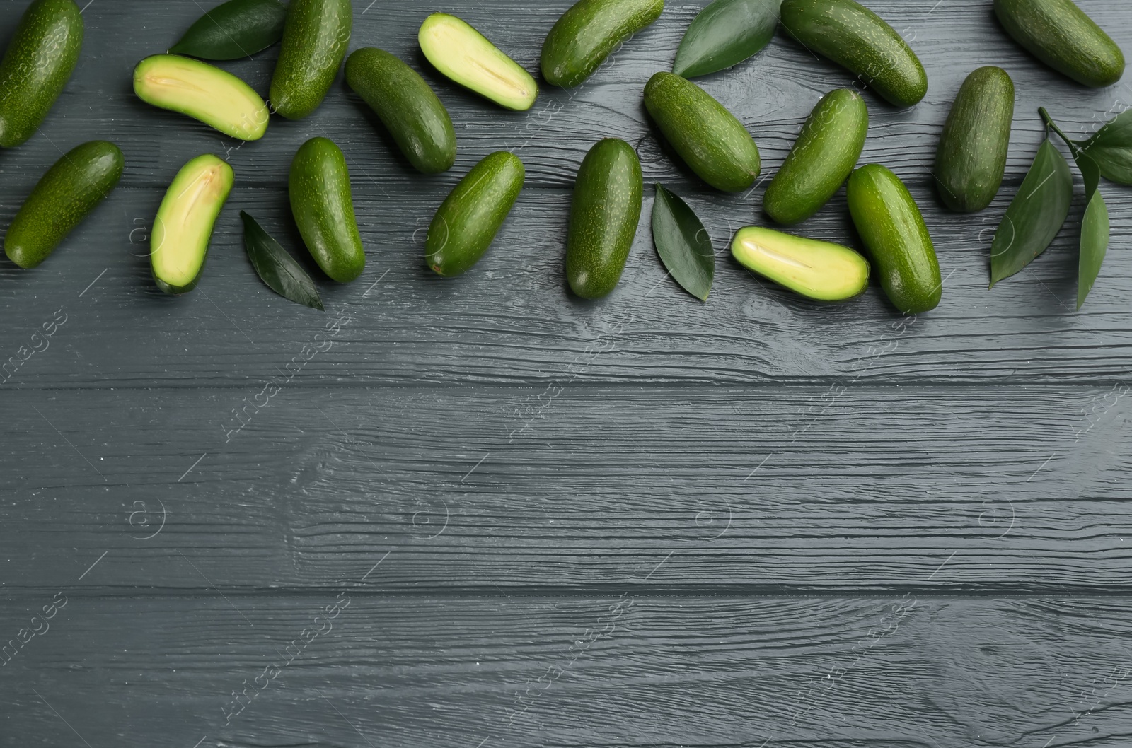 Photo of Fresh seedless avocados with green leaves on wooden table, flat lay. Space for text