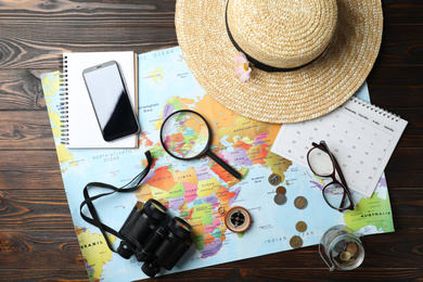 Photo of World map and items on wooden background, flat lay. Travel during summer vacation