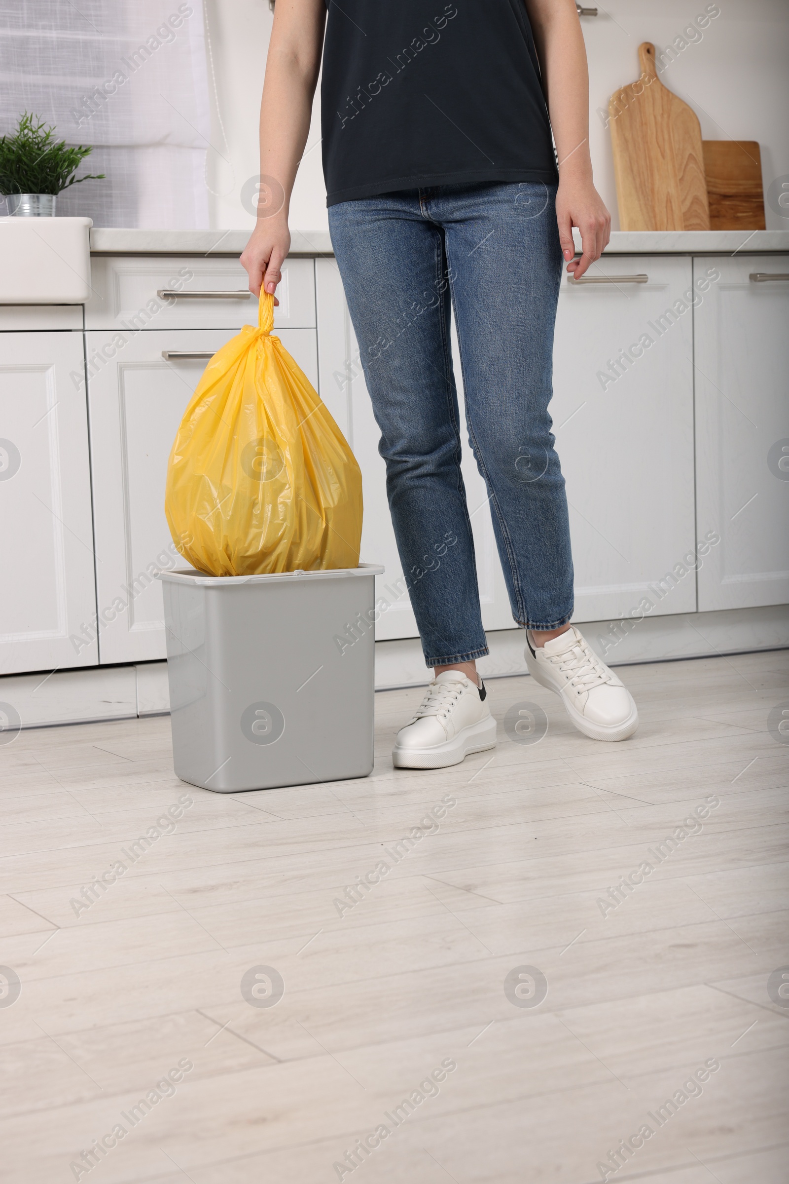 Photo of Woman taking garbage bag out of trash bin in kitchen, closeup