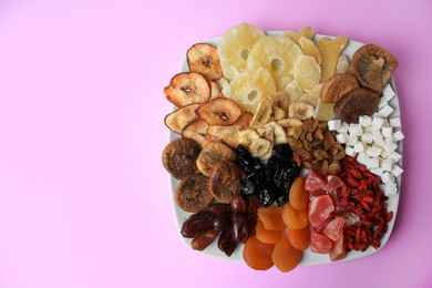 Photo of Plate with different dried fruits on violet background, top view. Space for text