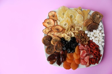 Plate with different dried fruits on violet background, top view. Space for text