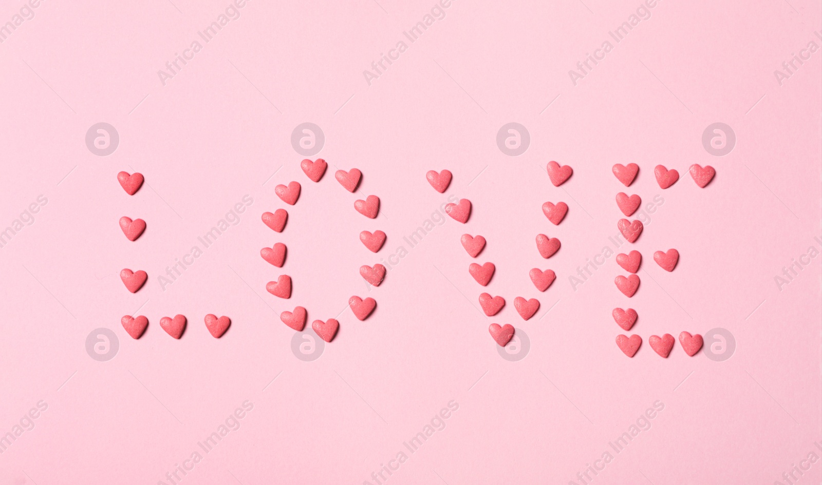 Photo of Word Love made with heart shaped sprinkles on pink background, flat lay