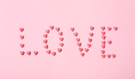 Photo of Word Love made with heart shaped sprinkles on pink background, flat lay