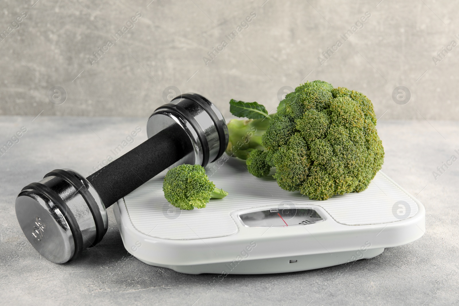 Photo of Healthy diet. Scale, broccoli and dumbbell on grey table