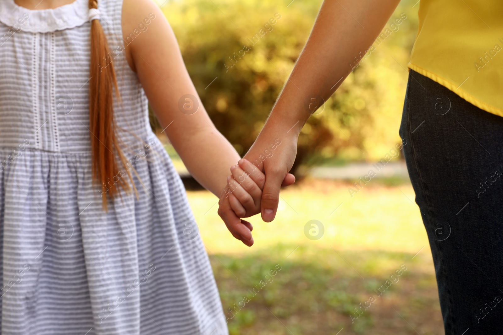 Photo of Little girl and her mother holding hands outdoors, closeup. Family weekend