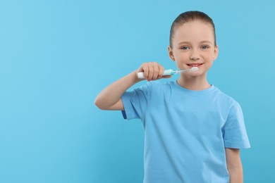 Happy girl brushing her teeth with electric toothbrush on light blue background. Space for text