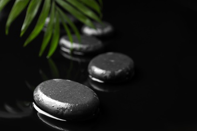 Photo of Composition with wet spa stones and green leaf on black background. Space for text