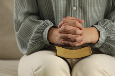 Photo of Religious woman praying over Bible on sofa, closeup