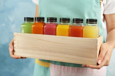 Woman holding wooden crate with tasty juices on color background