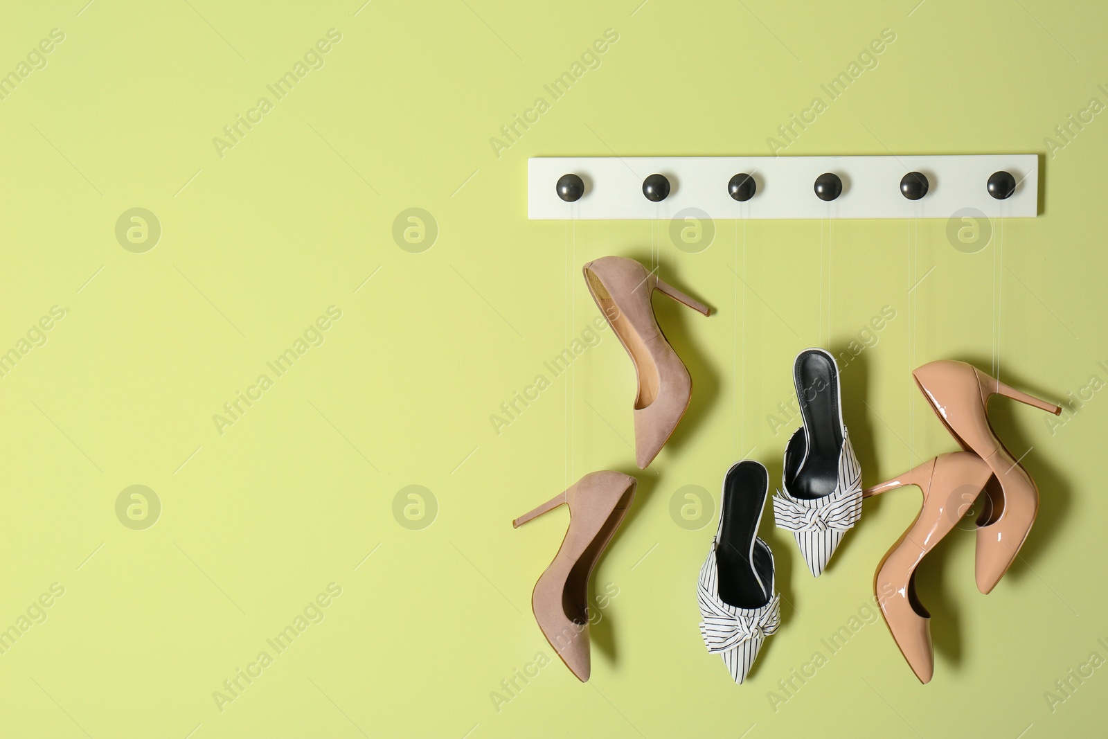 Photo of Different lady's shoes hanging on rack against color background, space for text