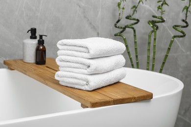 Photo of Stacked towels and personal care products on tub tray in bathroom