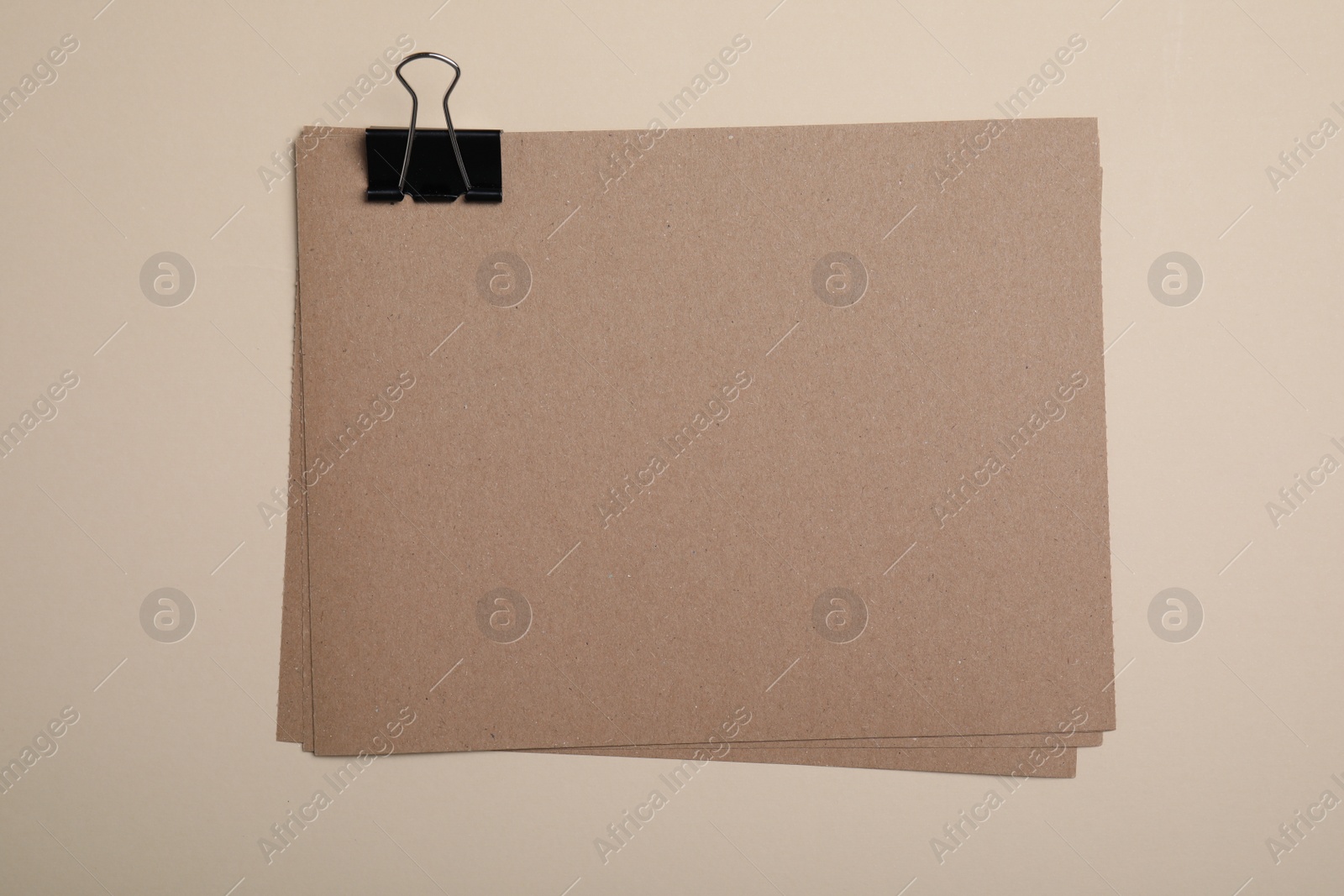 Photo of Sheets of brown paper with clip on beige background, top view