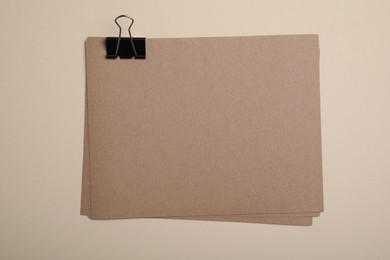 Photo of Sheets of brown paper with clip on beige background, top view