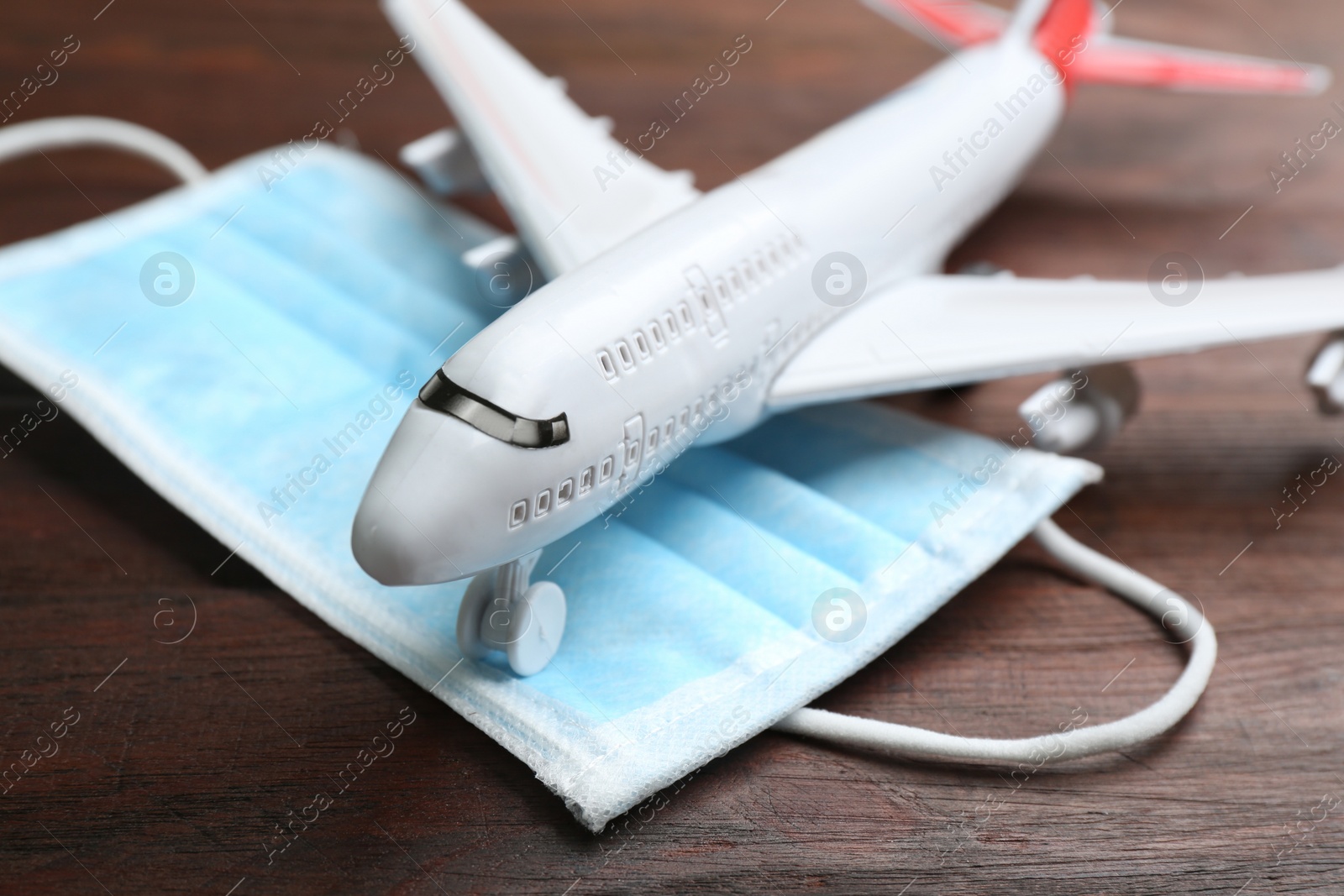 Photo of Toy airplane and medical mask on wooden background, closeup. Travelling during coronavirus pandemic