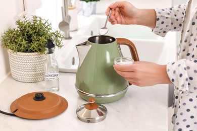 Photo of Woman adding baking soda into electric kettle in kitchen, closeup