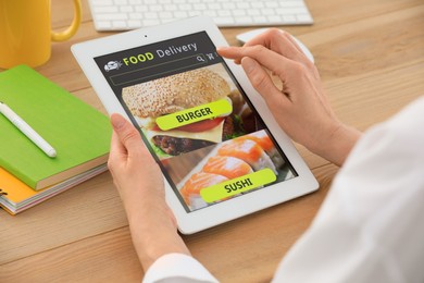 Photo of Woman using tablet for ordering food online at table indoors, closeup. Concept of delivery service