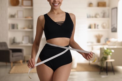 Photo of Young woman measuring waist with tape at home, closeup