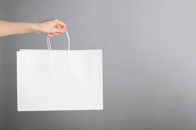 Photo of Woman holding white paper bag on grey background, closeup with space for text. Mockup for design
