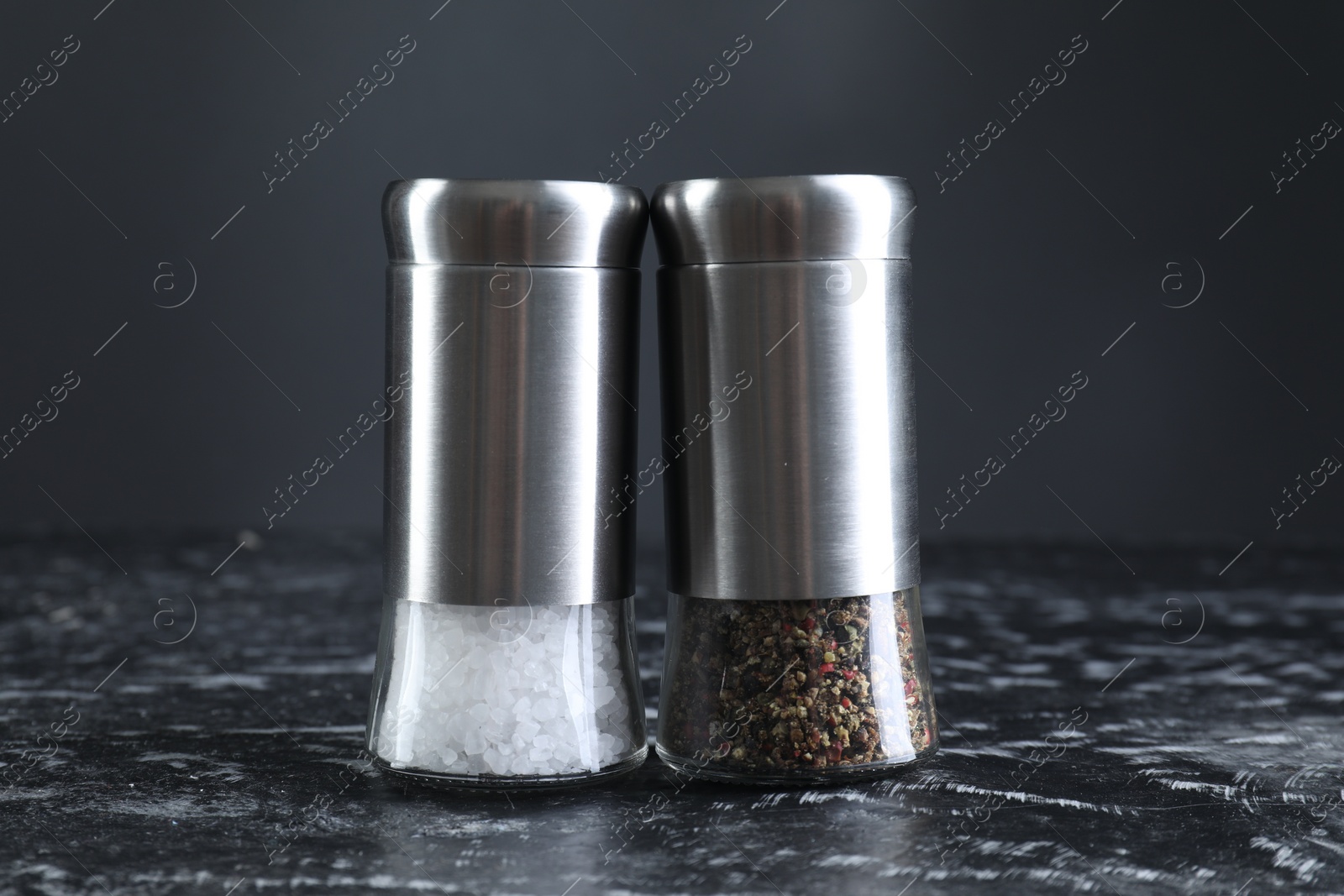 Photo of Pepper and salt shakers on dark marble table, closeup