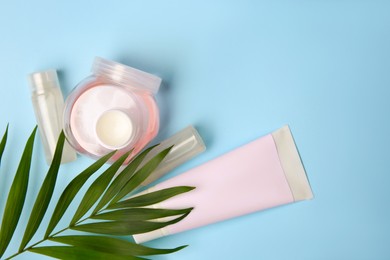 Cosmetic products and palm leaves on light blue background, flat lay