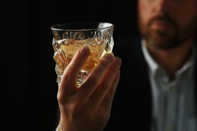 Man holding glass of whiskey with ice cubes on black background, selective focus